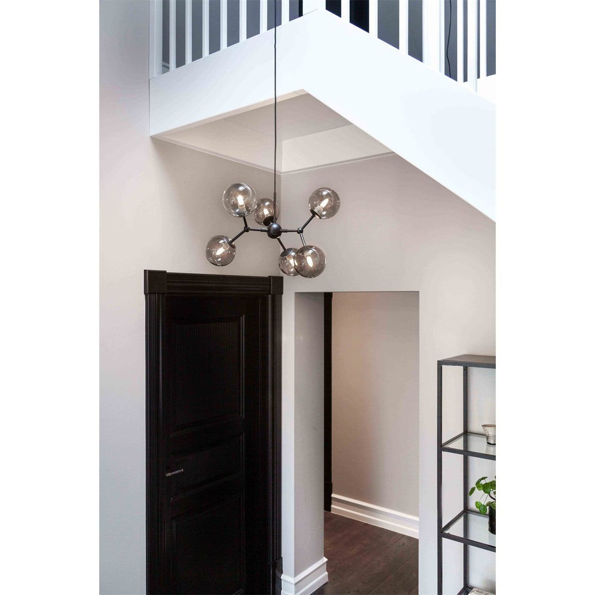 Atom Mini 6 Light Smoke Glass Chandelier in black, six smoked glass globes branching from a central hub, shown suspended in a hallway beneath a staircase.