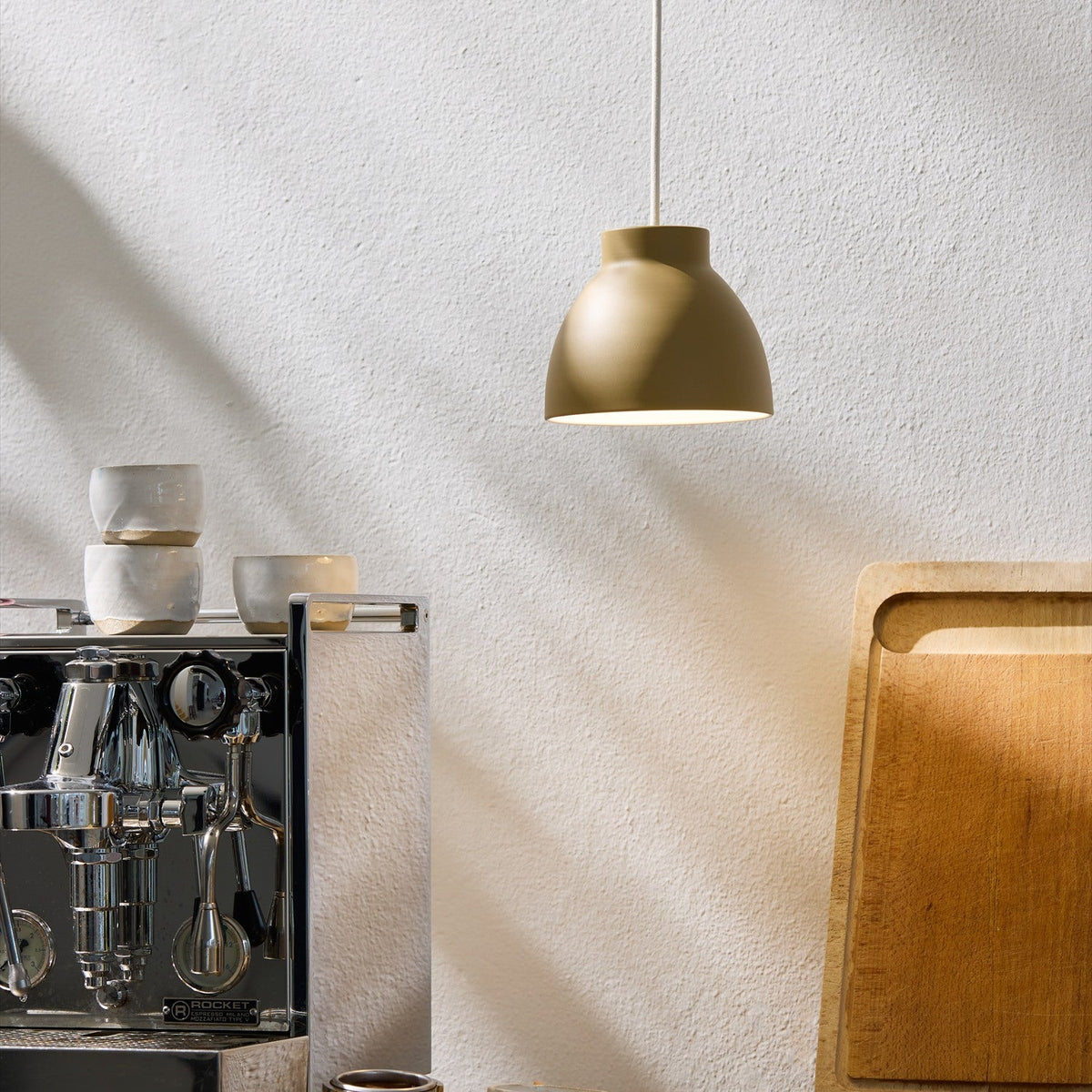 Object Pendant Light 16cm in latte beige metal with a stepped bell-shaped shade and white interior, hanging above a kitchen counter with an espresso machine and chopping board.