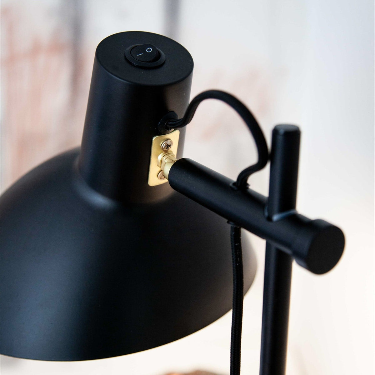 Close-up of the Metropole Floor Lamp in matte black, showing the rocker switch, brass mounting plate, adjustable knuckle joint, and fabric cable against a light background.