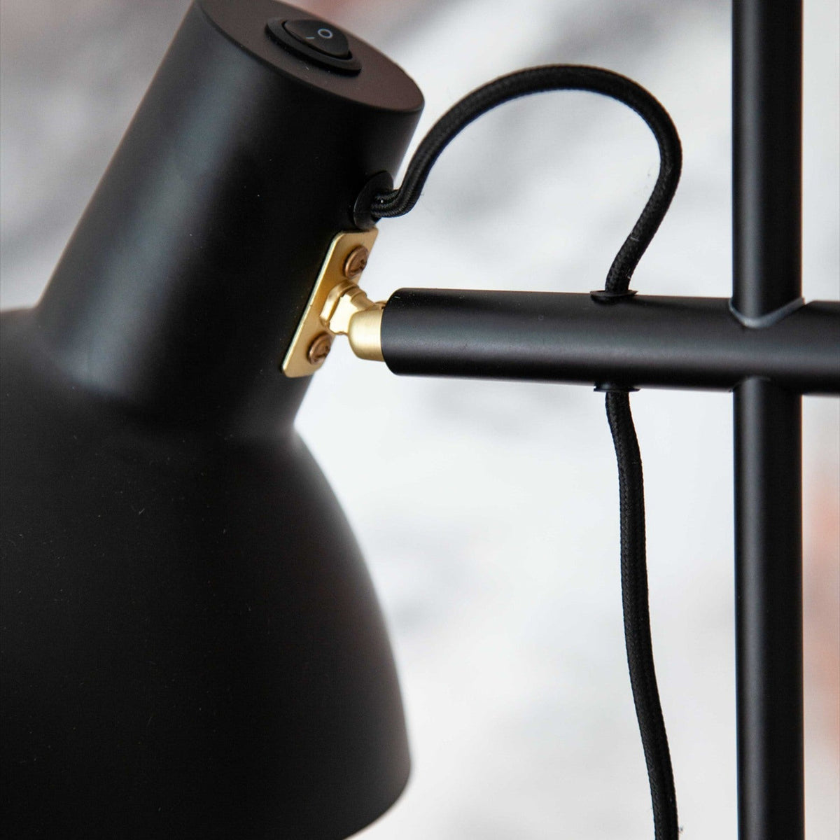 Close-up of the Metropole 2 Light Floor Lamp in black, showing a shallow dome shade with brass swivel joint, black rod arm, fabric cable, and switch.