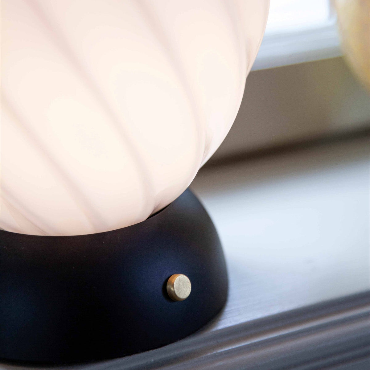 Close-up of the Twist Oval Table Lamp in opal and black, showing the ribbed glass egg shade meeting a black half-dome base with a brass control knob.