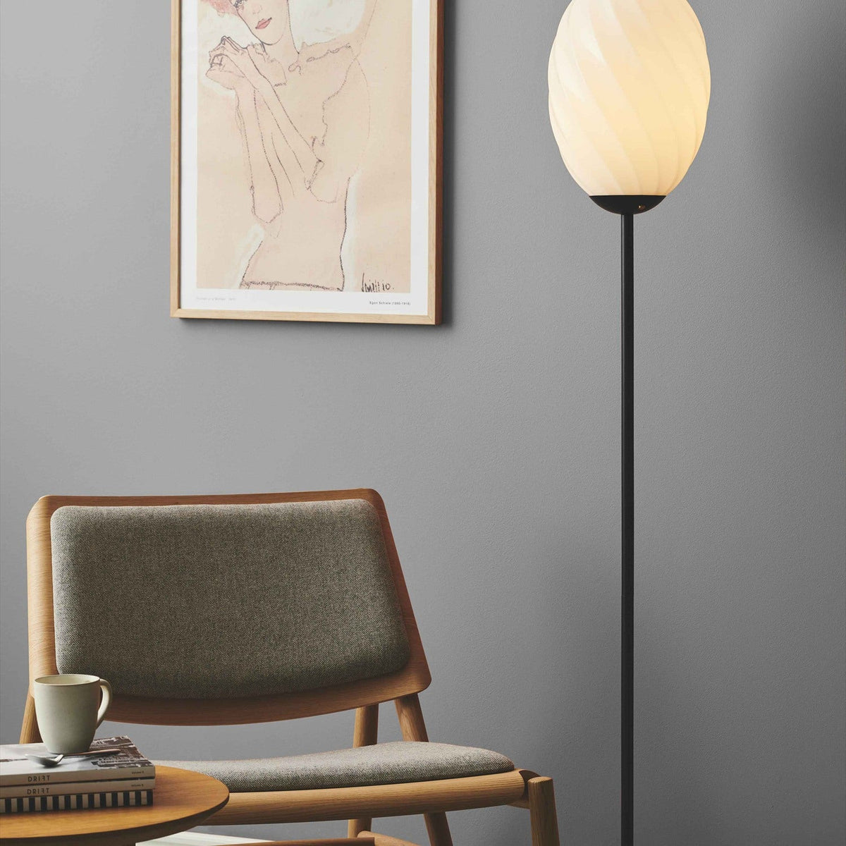 Twist Oval Floor Lamp in opal and black, twisted-flute glass shade on a slim black stem, shown beside an armchair and framed art in a living room.