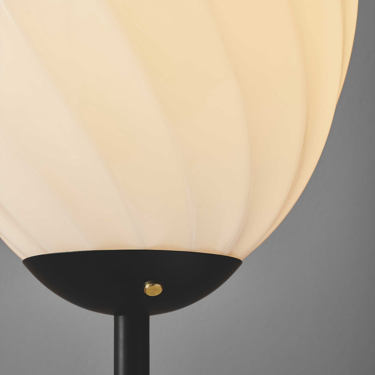 Close-up of the Twist Oval Floor Lamp in opal and black, showing the ribbed, twisted-flute glass shade meeting a matte black canopy with brass screw detail atop a slim black stem.