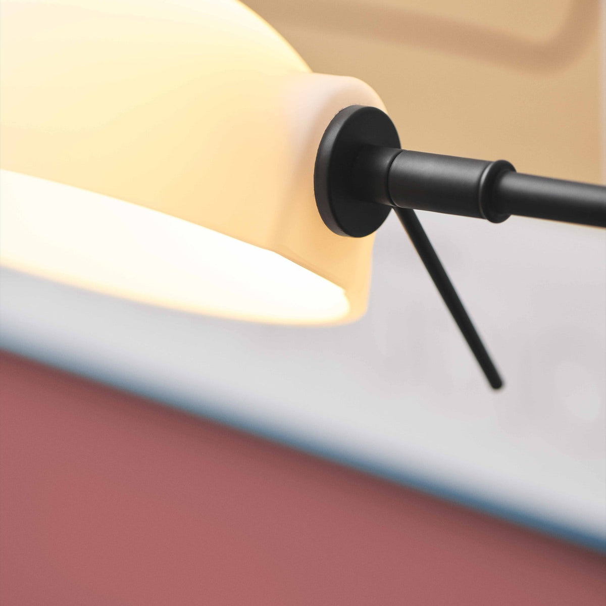 Copenhagen Wall Light in black, close-up of the round wall plate, jointed arm and knuckle, with the white half-dome shade glowing softly.
