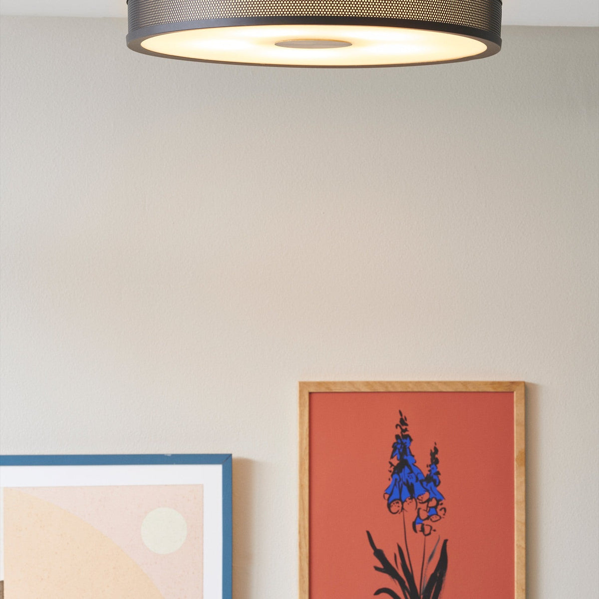 Frame 5 Light Flush Ceiling Light 43cm in black with perforated mesh drum and antique brass centre boss, shown lit above a wall with framed art prints.