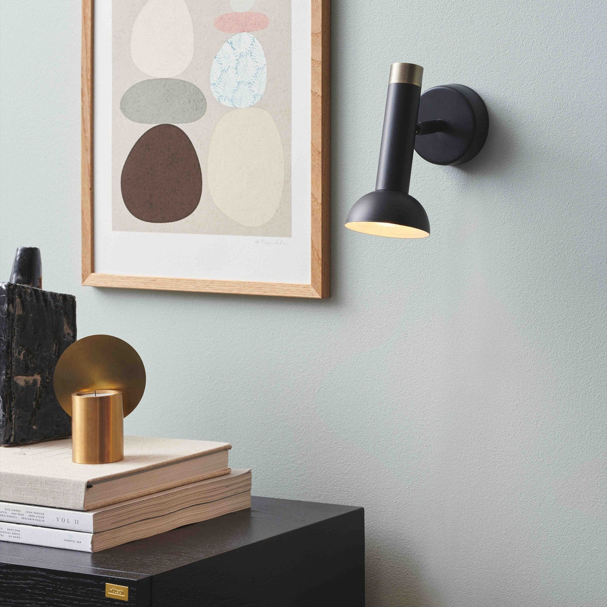 Torch Wall Pendant Light in black and antique brass, angled tube with brass collar and downward dome shade, mounted above a nightstand near framed abstract art.