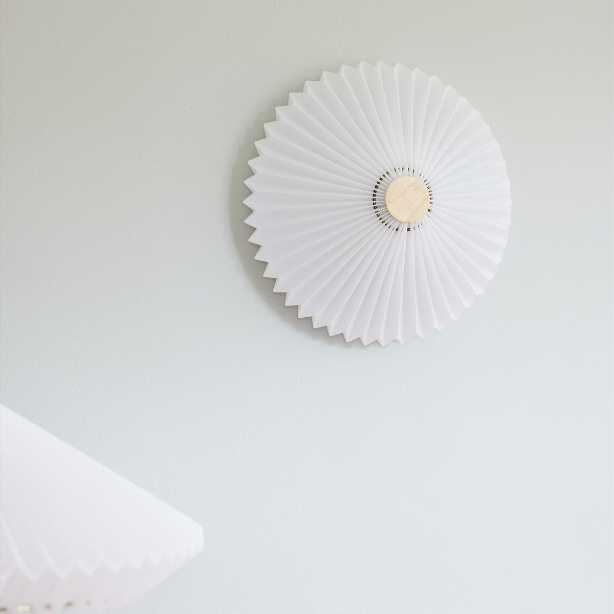Paris Clean Flush Ceiling Light 50cm in white pleated paper with a round antique brass centre disc, mounted on a light grey wall beside a second pendant edge.