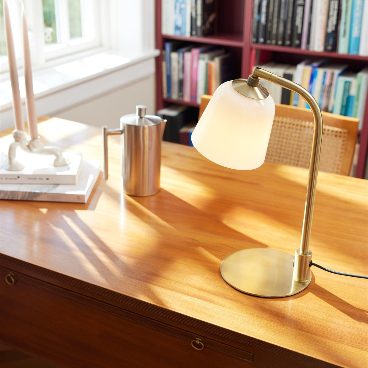 Room table lamp with opal glass bell shade on a curved antique brass arm and round base, shown lit on a wooden desk in a study.