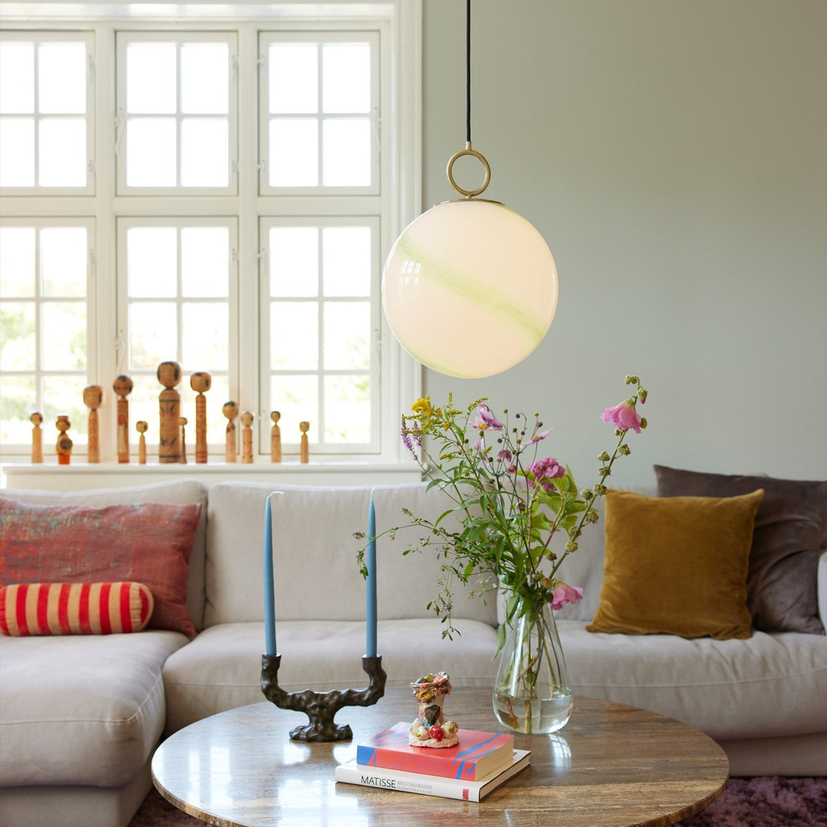 Stockholm Pendant Light 30cm in Marble Green, a round opal glass globe with green marbled streaks hung from a brass ring, shown above a coffee table in a living room.