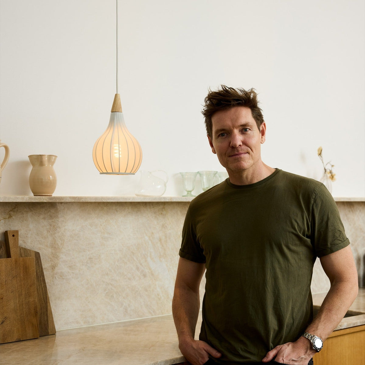 Drops Textile Pendant Light 17cm in White with onion-shaped ribbed shade and wood cap, hanging above a marble kitchen counter beside a man in an olive T-shirt.