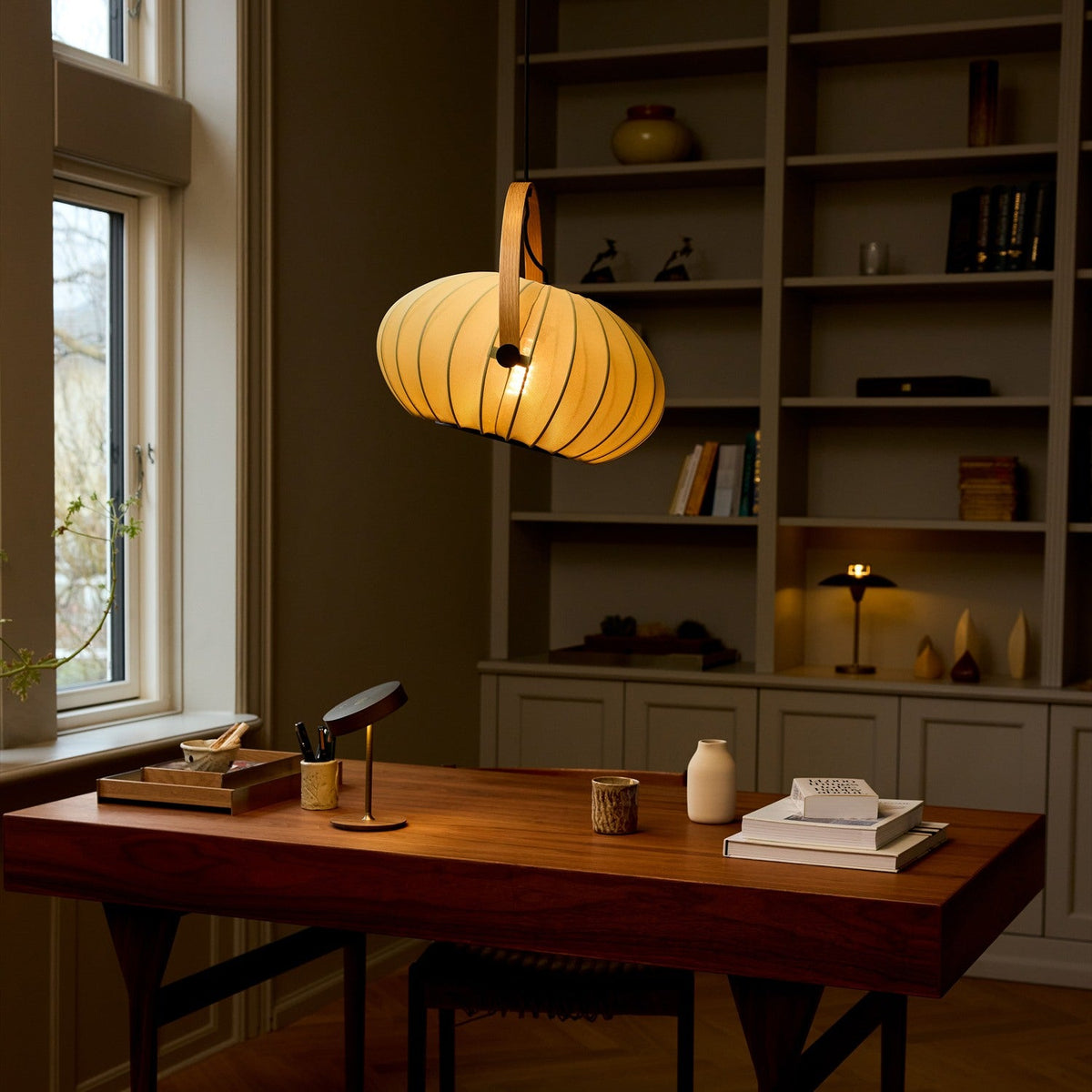 DC Textile Forest Pendant Light 40cm in green, ribbed fabric shade with pale wood arched handle, shown lit above a wooden desk in front of a bookshelf.