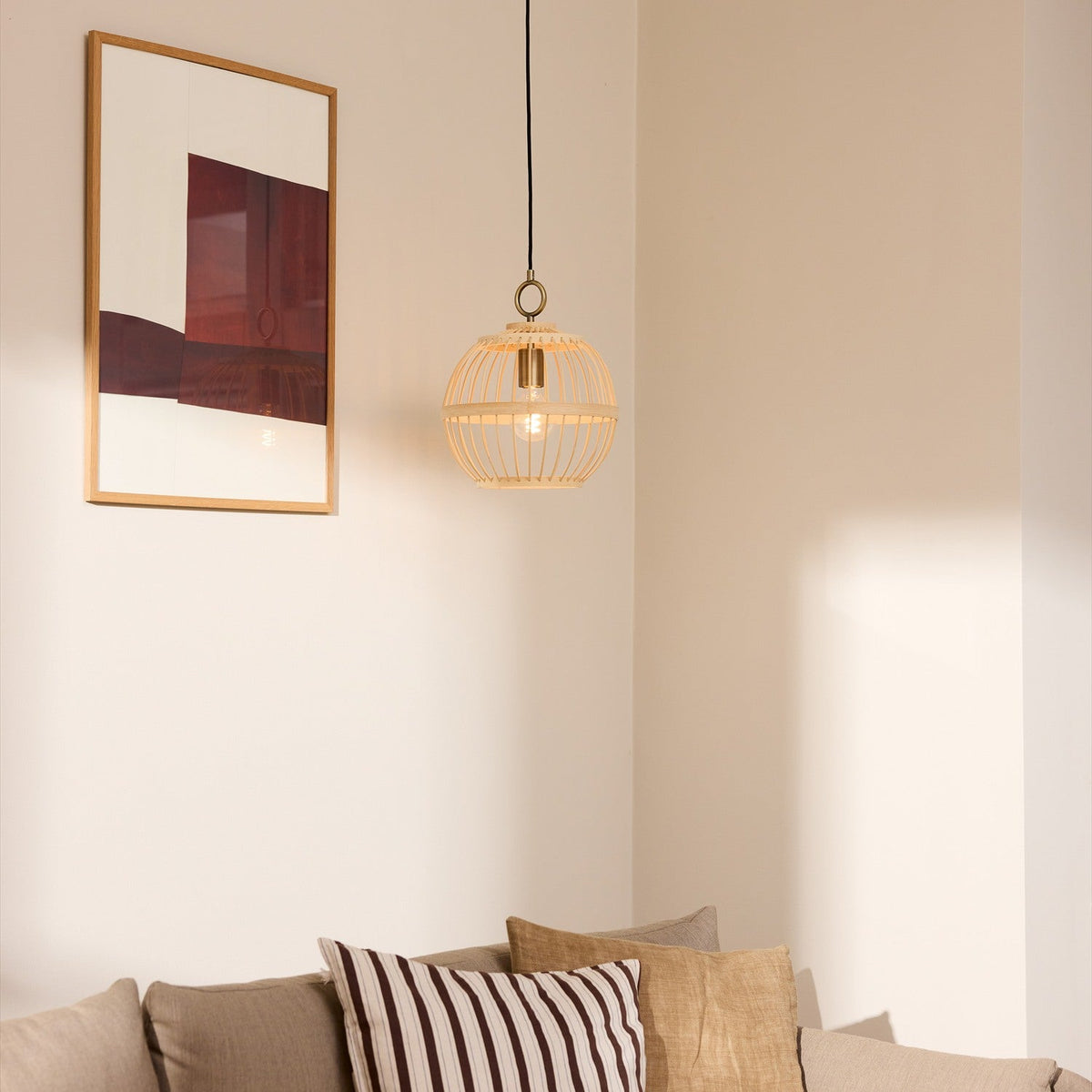 Stockholm Nordic Edition Pendant Light 30cm in natural bamboo with brass collar, shown hanging in a corner above a sofa beside a framed wall art.