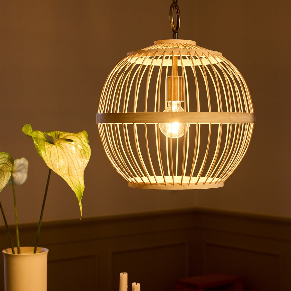 Stockholm Nordic Edition Pendant Light 40cm in natural bamboo, a round woven cage with a visible bulb, hung above a dining table in a warm-toned room.