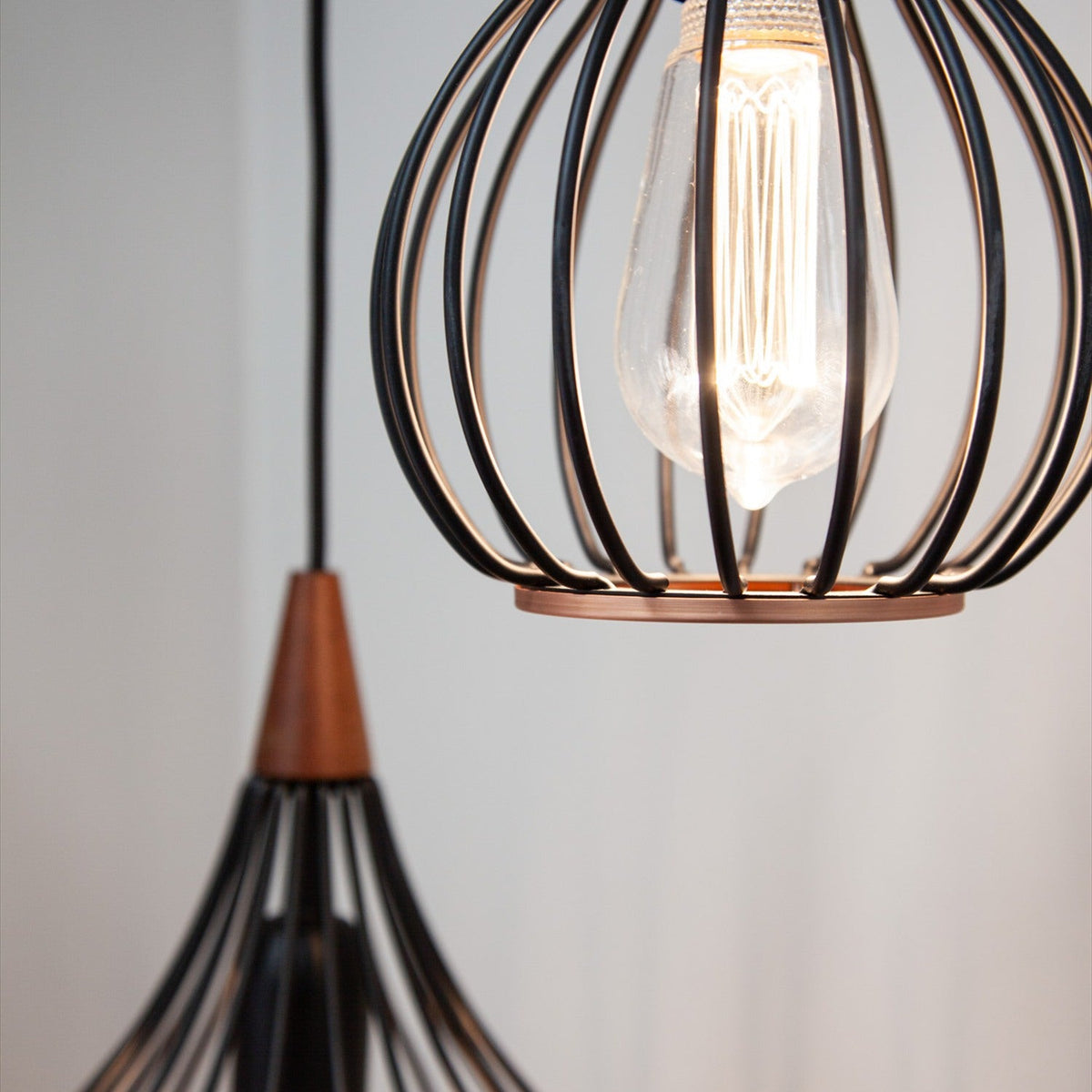 Drops Pendant Light 30cm in black wire cage design with dark wood cap and copper base ring, shown beside a globe pendant with visible bulb against a light grey background.