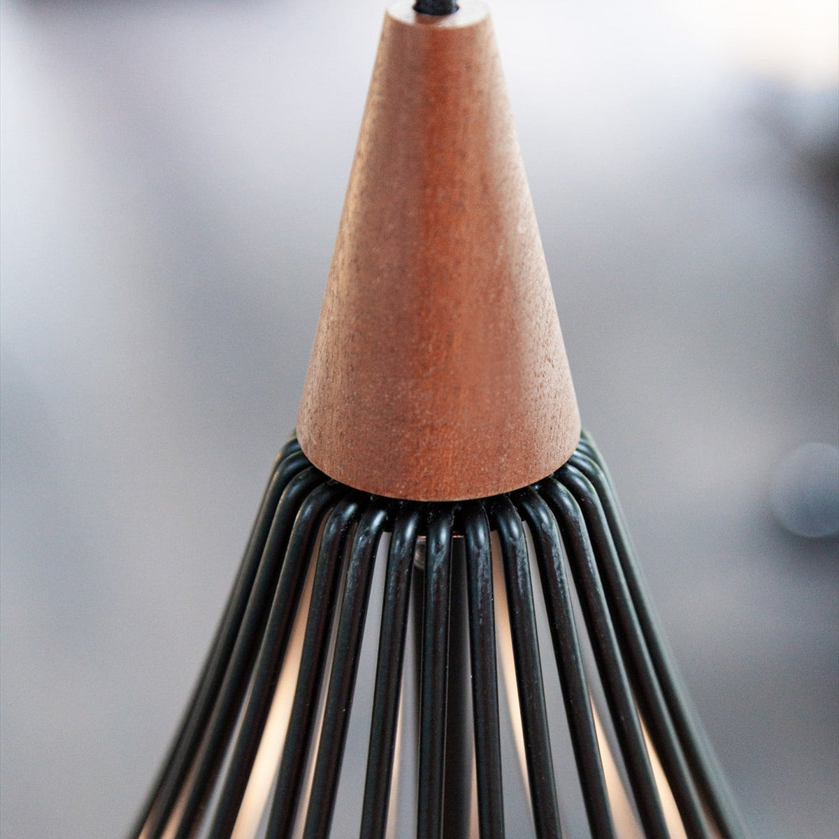 Close-up of the Drops Pendant Light 38cm, showing the dark wood cone top and black wire ribs forming an open teardrop cage, against a blurred neutral background.