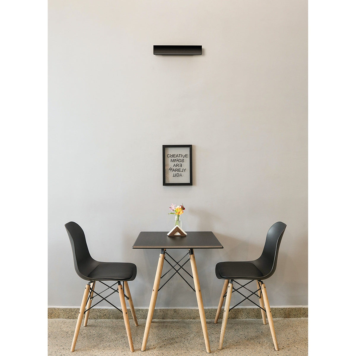 Hanok 41cm linear LED wall light in matt black mounted horizontally above a framed print, with a small dining table and two chairs below.
