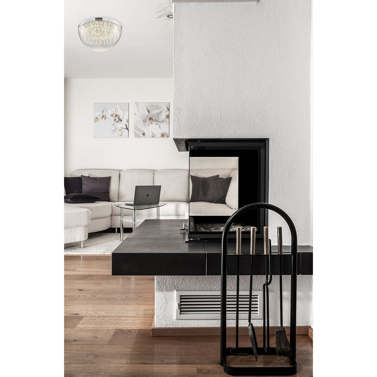 Diyas Harper Large LED crystal flush ceiling light in polished chrome illuminates a modern living room with white sofa and black fireplace surround.