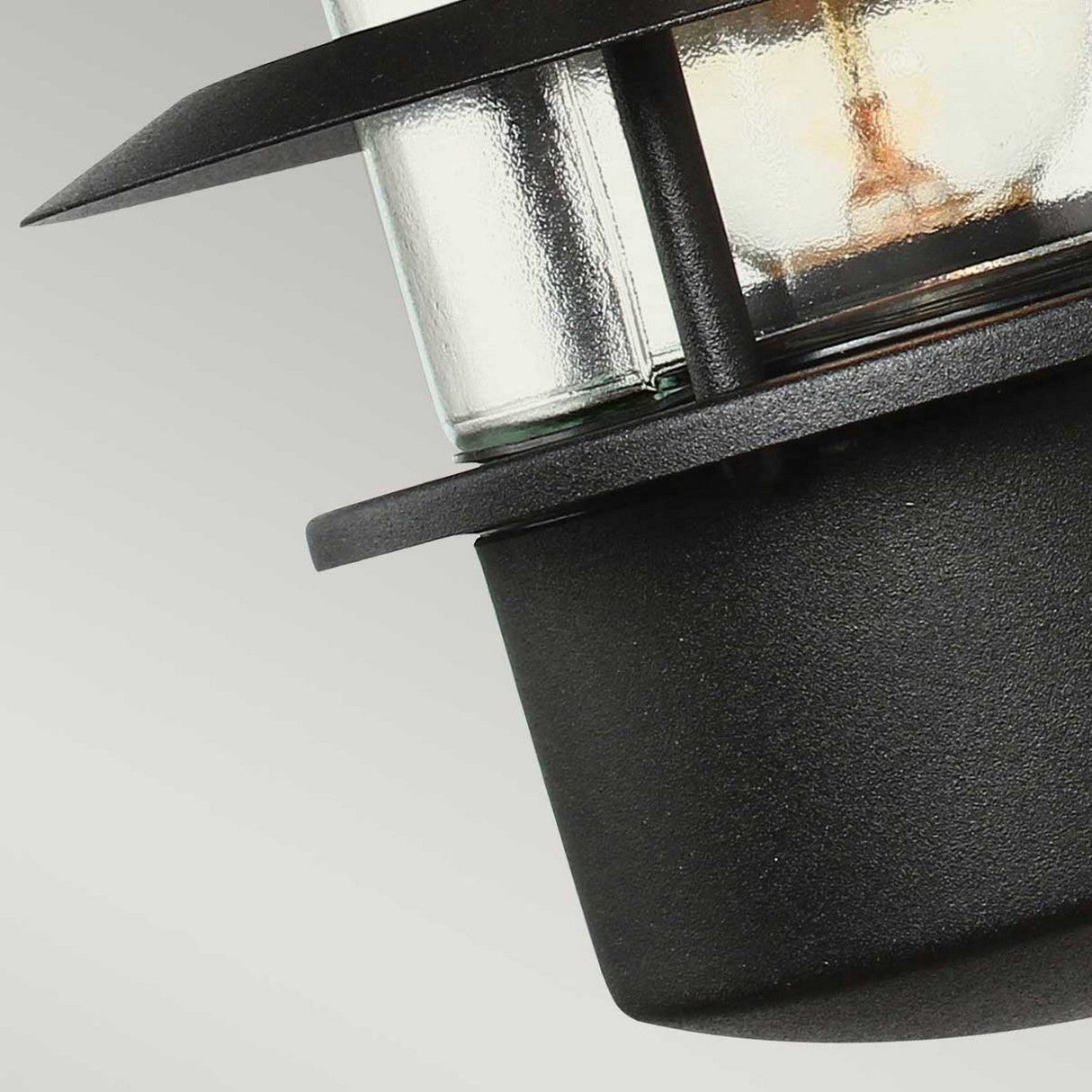 Close-up of the Helsingor 1 Light Outdoor Wall Light in black, showcasing a Danish-inspired design with a glass cylinder encased in metal rings. The background is a plain light gray.