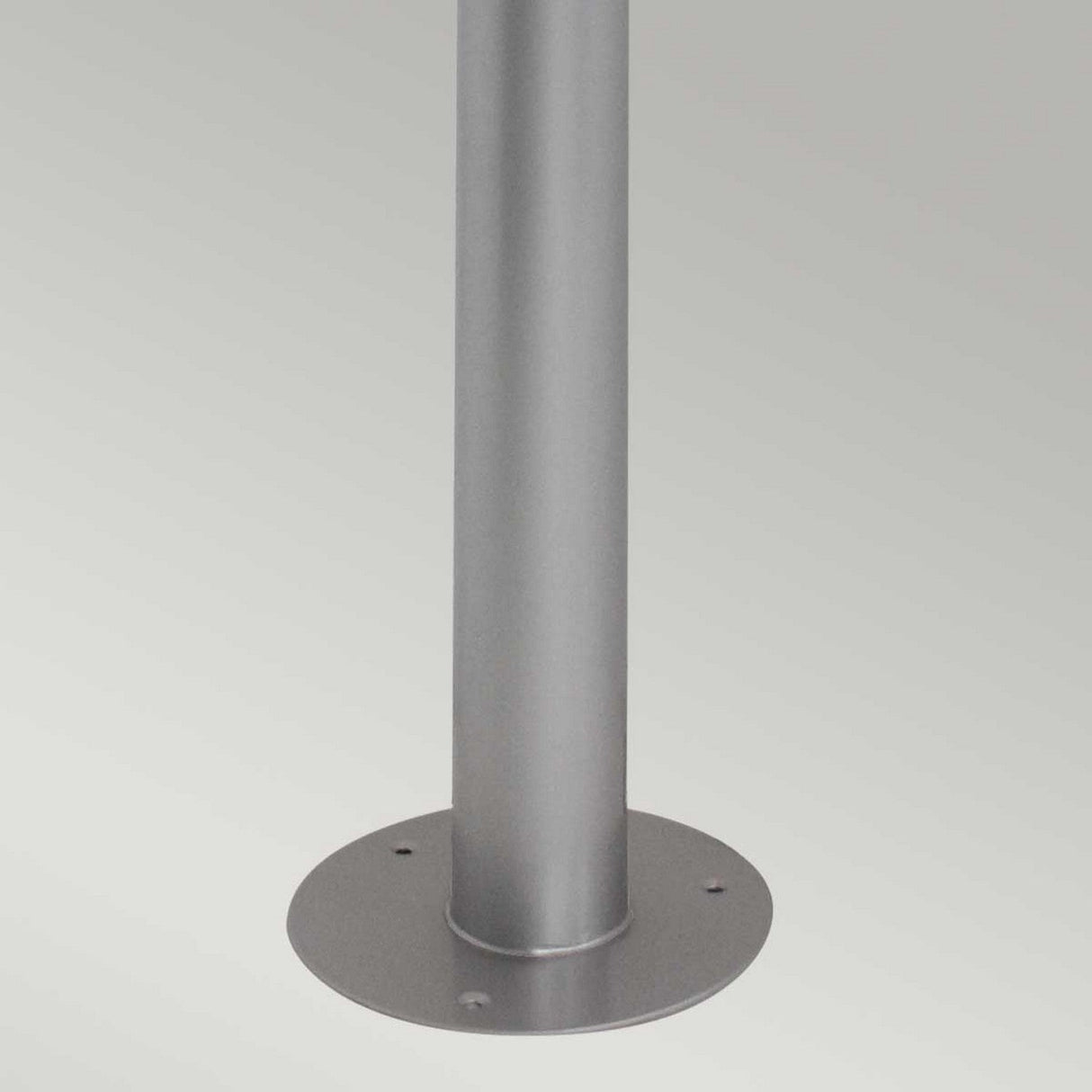 The Helsingor 1 Light Bollard Lantern - Silver is mounted vertically on a flat surface with its round Scandinavian-inspired base featuring three holes for secure placement. This bollard lantern elegantly combines functionality and style against a plain light gray background.