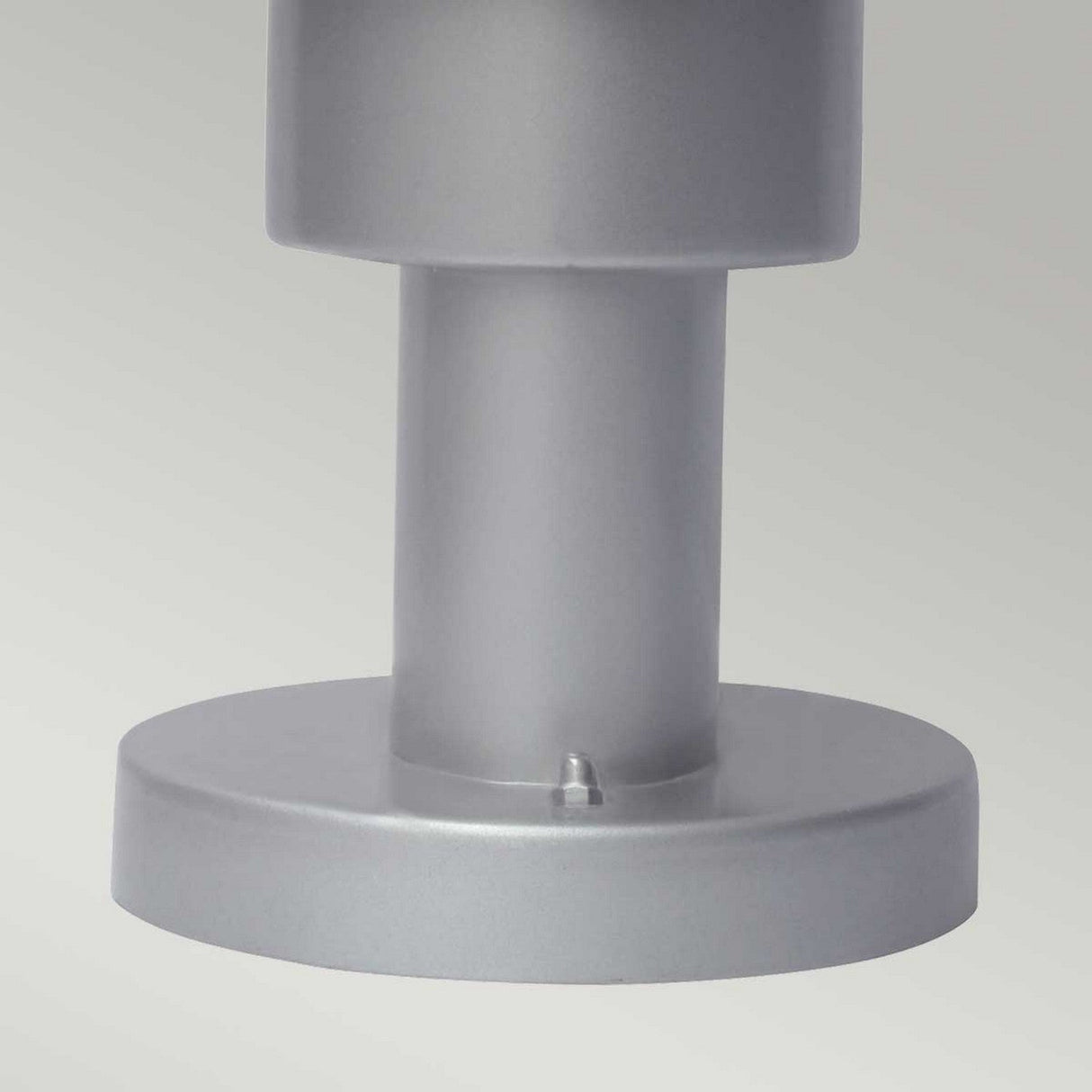 A close-up view of the Helsingor 1 Light Pedestal Light in silver showcases its stainless steel cylindrical form and round base, potentially part of a larger structure or machine. The smooth, gray surface exhibits subtle shadows, while its IP44 rating indicates it is durable for outdoor conditions. The backdrop is a light, neutral hue.
