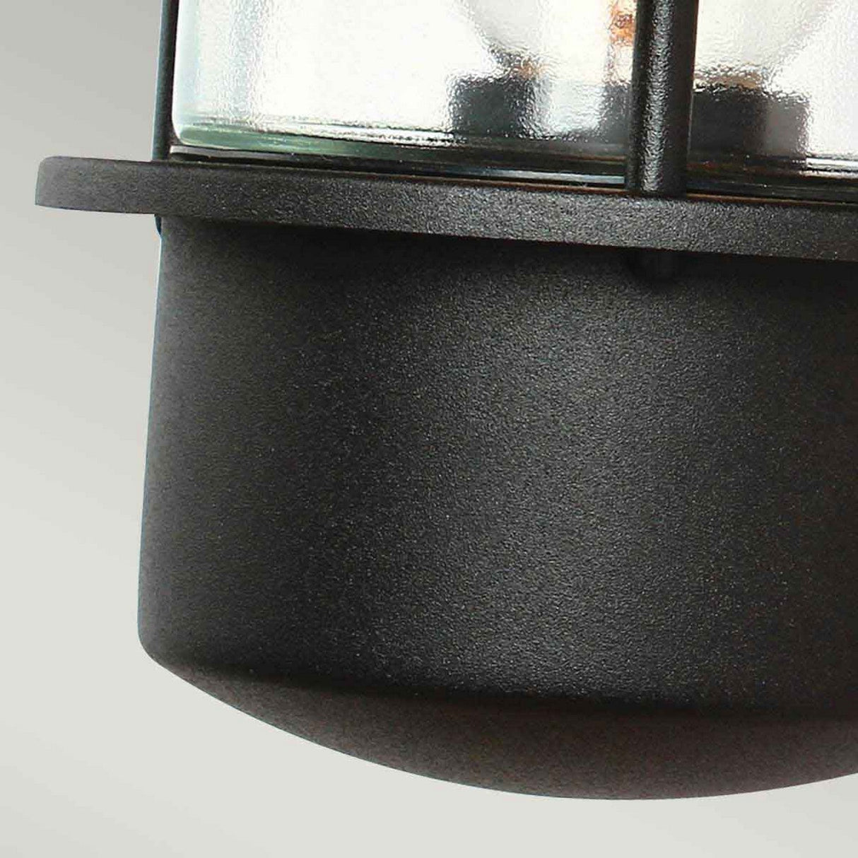 The Helsingor 1 Light Outdoor PIR Wall Light in black showcases a clear glass cover, visible screws, and metal bars in an industrial style. This weather-resistant exterior lighting stands out against a gradient of light gray, making it the ideal choice for outdoor spaces.