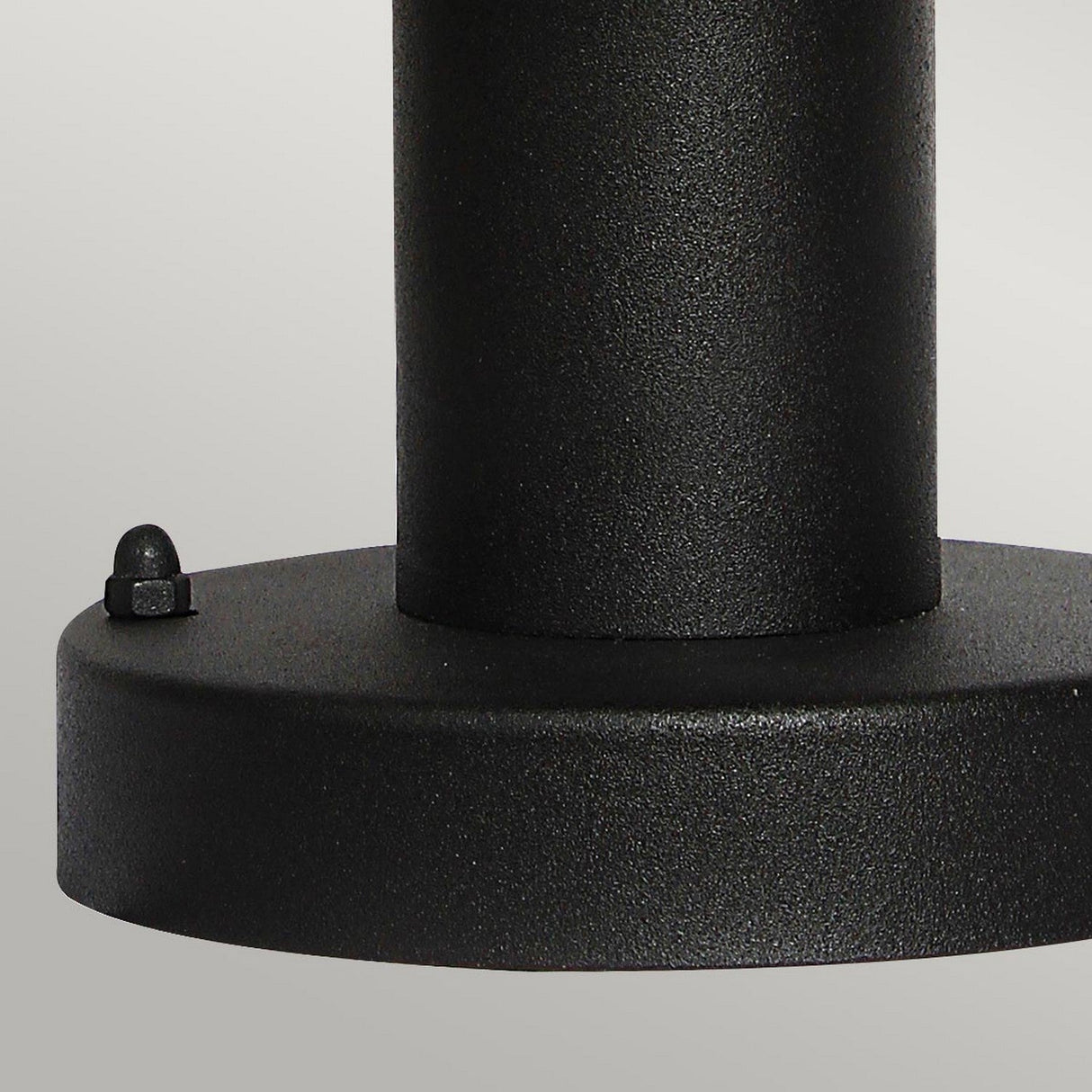 Close-up of the Helsinor 1 Light PIR Pedestal Light in black, featuring a textured cylindrical body with a flat, circular base. Set against a plain, light gray background, this object exudes a sleek and modern appearance.