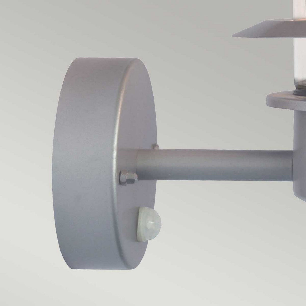 Close-up of a contemporary Helsingor 1 Light Outdoor PIR Wall Light - Silver, featuring a cylindrical metal base and an angled arm that supports the light. The design boasts a sleek, minimalist aesthetic set against a light gray background, providing both stylish flair and improved security lighting.