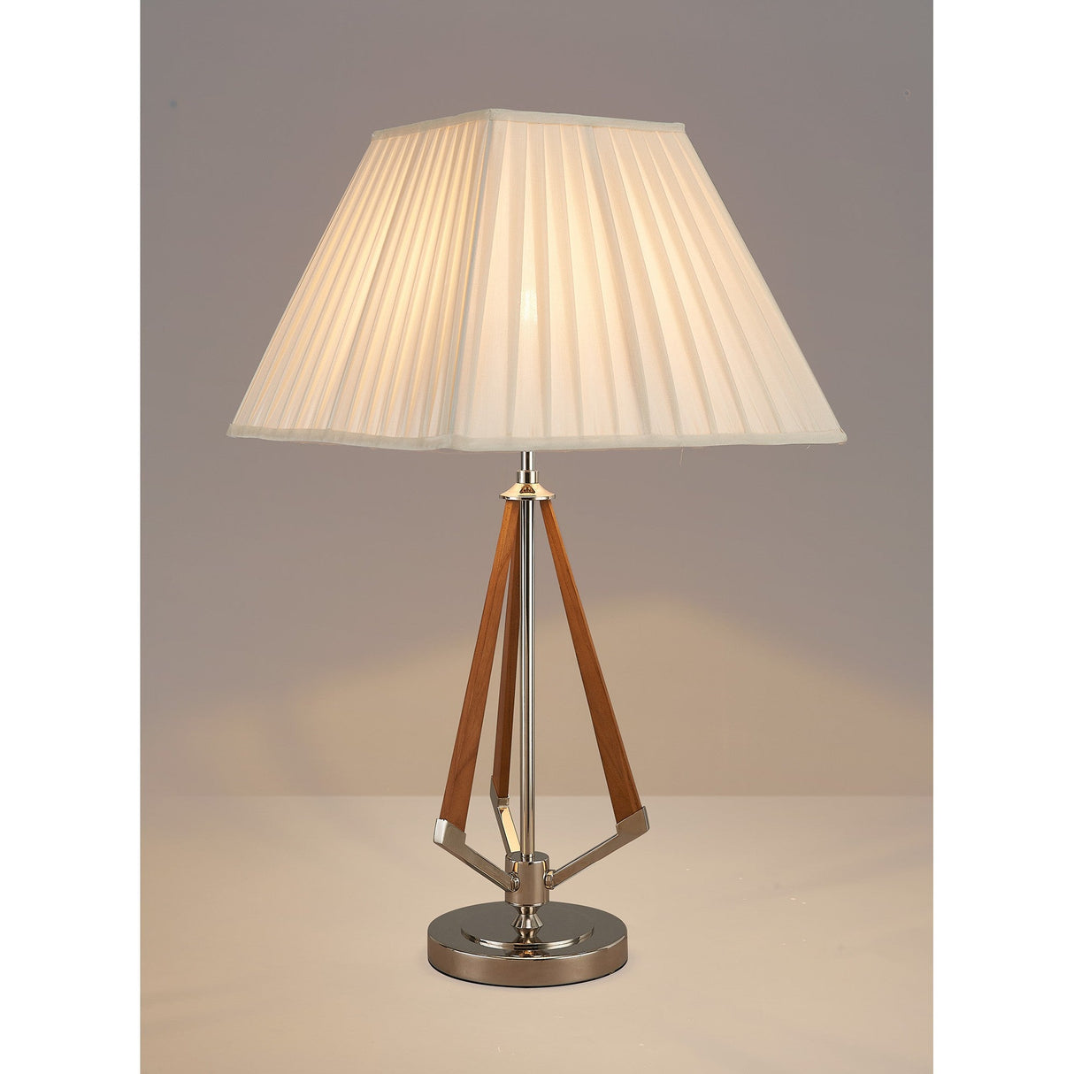 The Hilton 1 Light Wood Table Lamp features a pleated ivory shade, nickel circular base, taupe accents, and wooden triangular supports. Lit and displayed on a neutral surface against a plain background.