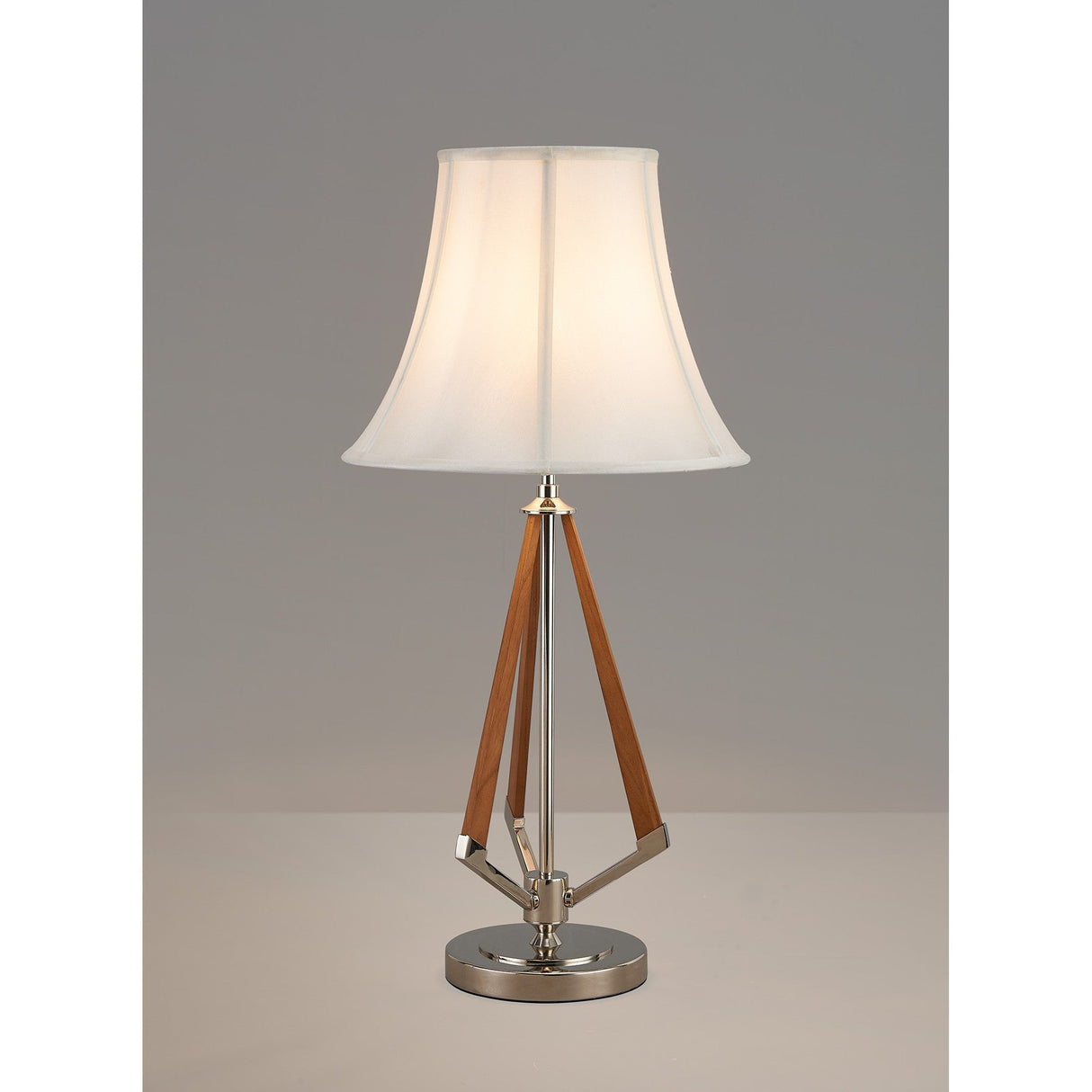The Hilton 1 Light Wood Table Lamp features a nickel base, cream shade, and three angled wooden legs in a triangular design. Lit against a plain gray background, it adds modern charm to any space.