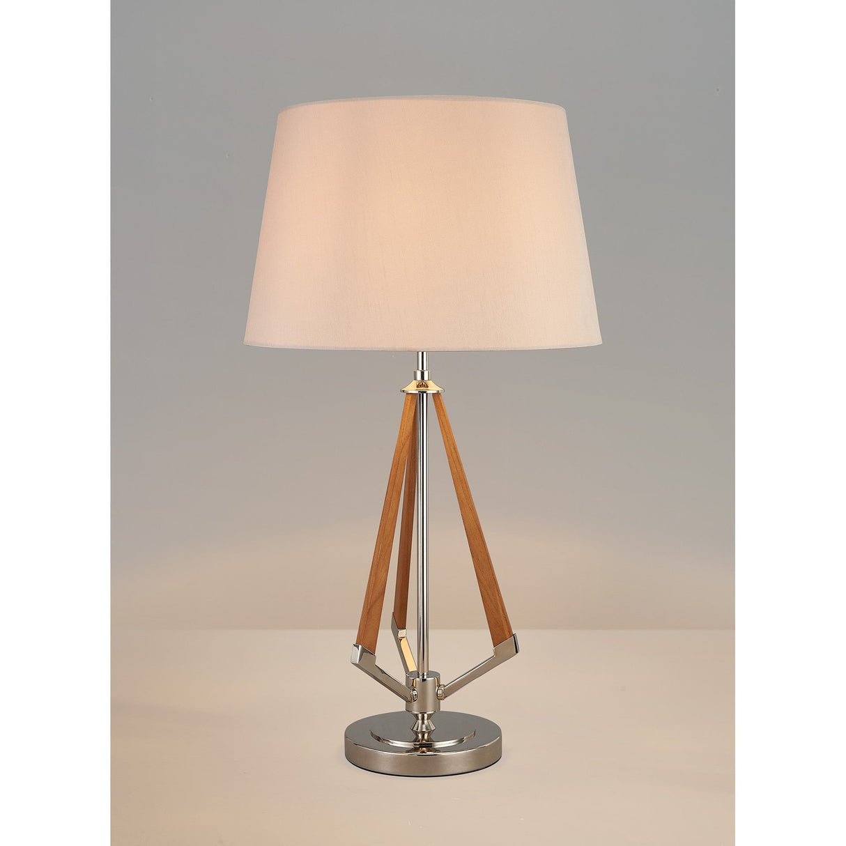 The Hilton 1 Light Wood Table Lamp features a nickel and wood triangular base with a nude beige fabric shade, shown against a plain light gray background.