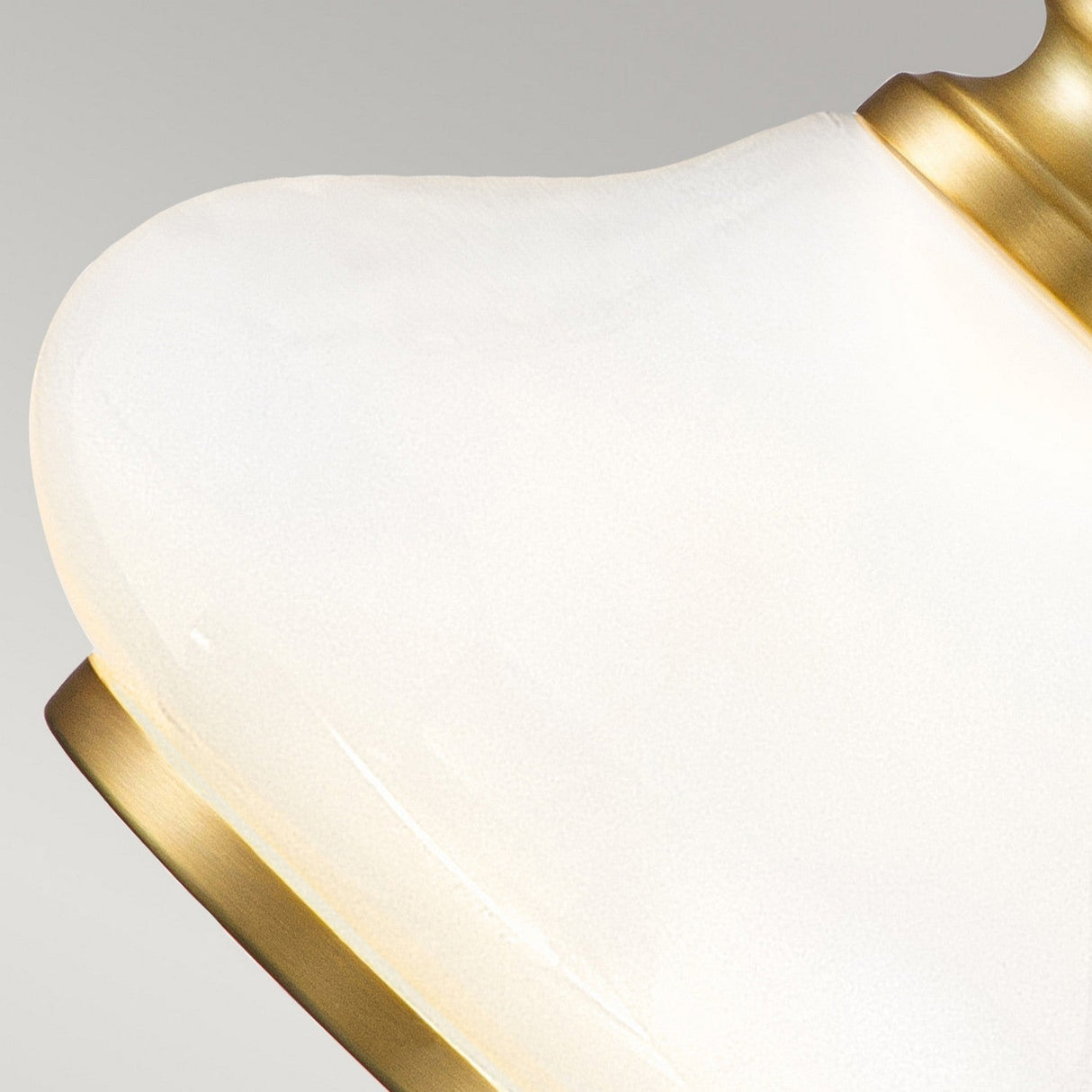 Close-up of the Ainsley 1 Light Wall Light with an opal glass shade, featuring a smooth, frosted texture and framed by a brushed brass edge. The neutral background highlights the energy-efficient LED lamp's elegant design.