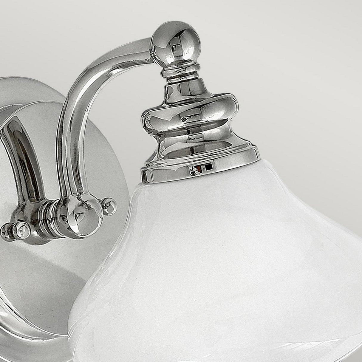 Close-up of the Ainsley 1 Light Wall Light in polished chrome, showcasing its curved arm and opal glass bell-shaped shade, set against a plain background.