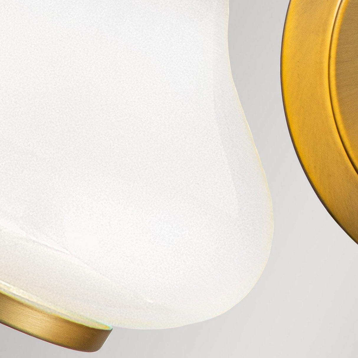 Close-up of the Ainsley 2 Light Wall Light in brushed brass, showcasing its modern LED lamp with an opal glass shade. The smooth, curved design of the shade pairs beautifully with the elegant metallic touch. A neutral gray background enhances its sophisticated charm.