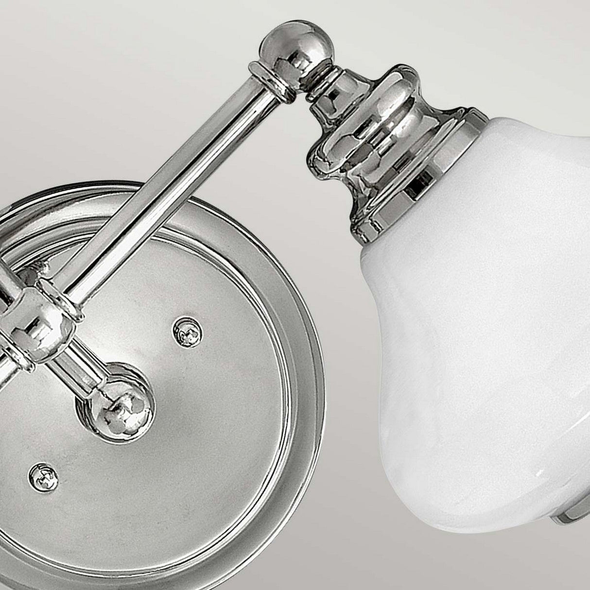 Close-up of the Ainsley 2 Light Wall Light - Polished Chrome, showcasing its polished chrome base and opaque white glass shade. The design includes sleek, modern lines with a circular metal plate mounted to the wall, featuring energy-efficient LED lamps.