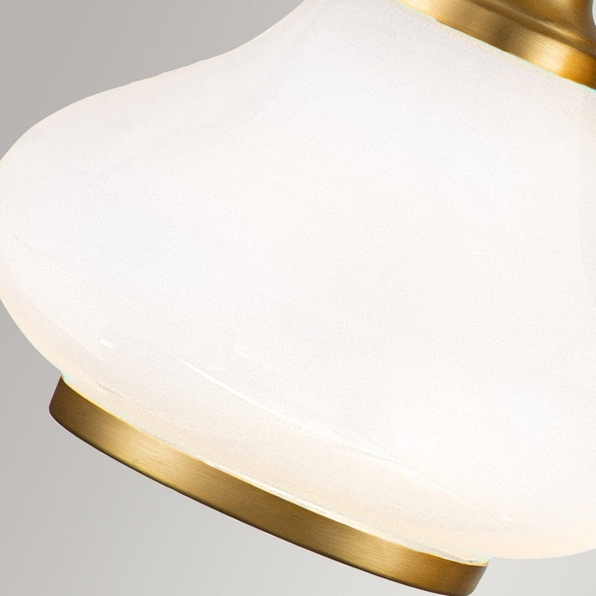 Close-up of the Ainsley 3 Light Wall Light in brushed brass with a frosted glass fixture. The brass trim outlines the smooth, curved edge of the opal glass shade, set against a neutral background.