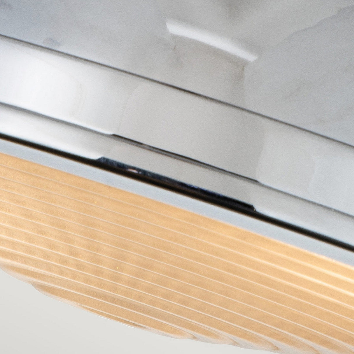 A close-up of the Amelia 2 Light Flush Light showcases its modern design, featuring a smooth polished chrome finish and a ribbed cast glass diffuser. Its sleek, minimalist style highlights the interplay of textures and materials.