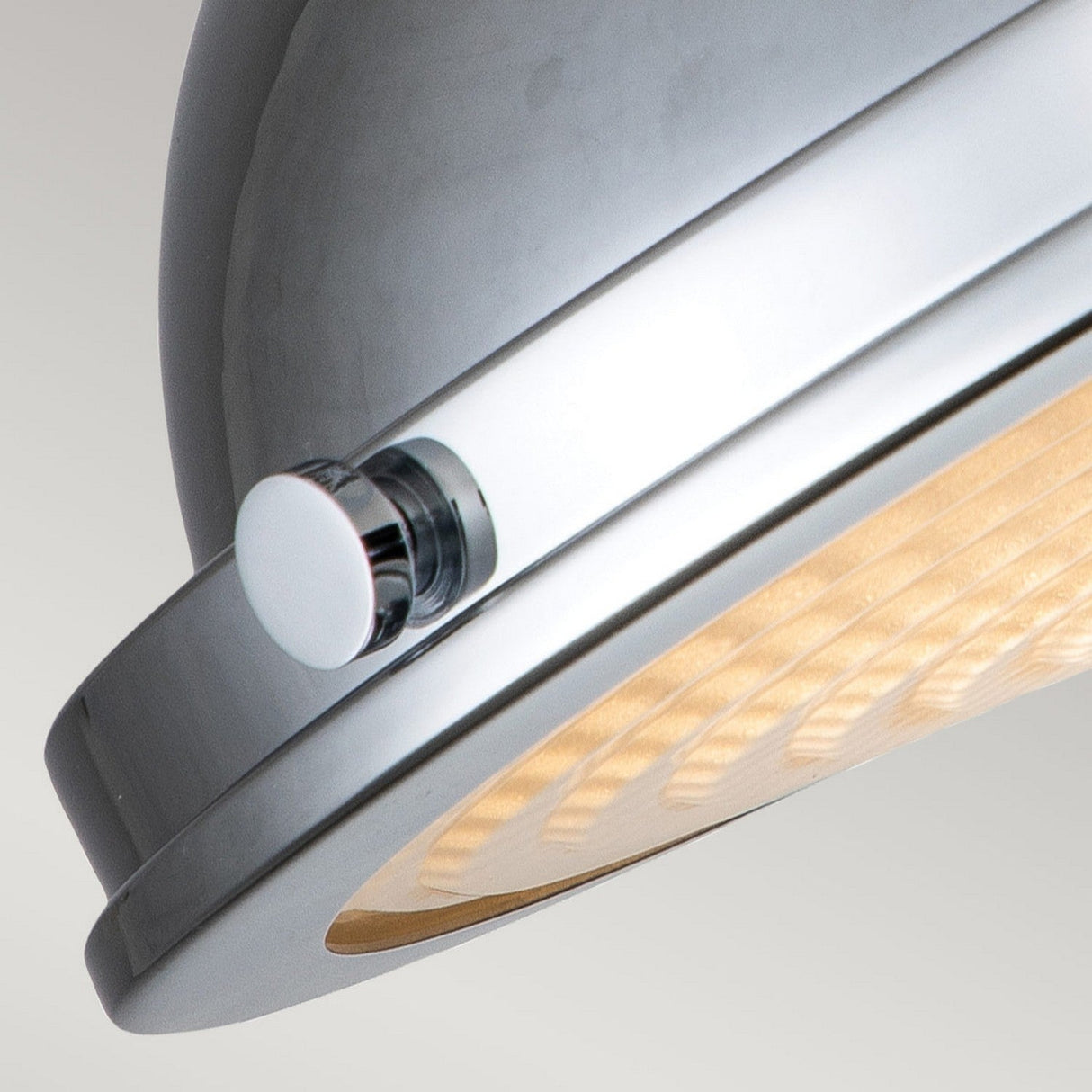 Close-up of the Amelia 2 Light Flush Light, showcasing its metallic dome shape and circular grid pattern that emits a warm glow. This modern fixture boasts a polished chrome finish along with a small, round switch on the side, all set against a neutral gray backdrop to accentuate its sleek design.
