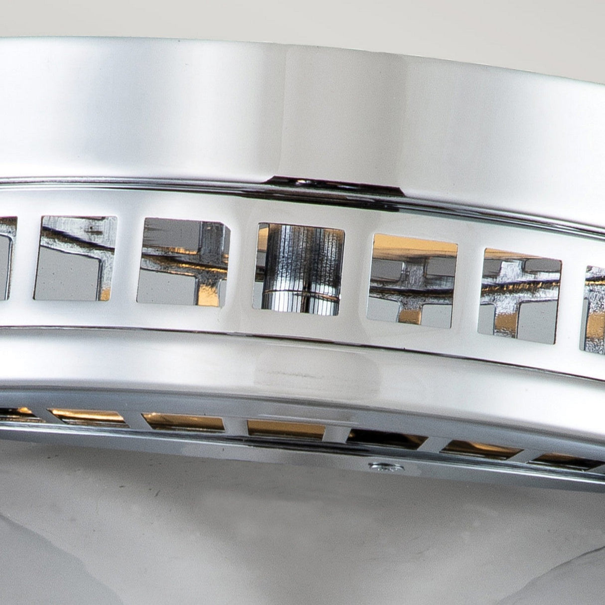 Close-up of the Amelia 2 Light Flush Light in polished chrome, showcasing its modern design with rectangular cutouts along the edge. The gleaming finish beautifully reflects light, which shines through the openings. As an elegant and stylish addition to any room, this contemporary light fixture embodies refinement.