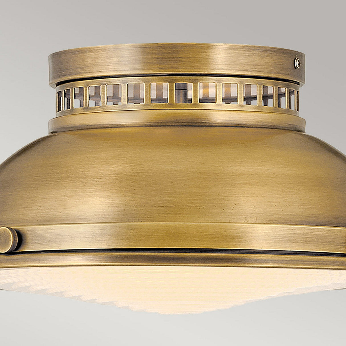 Close-up view of the Amelia 2 Light Flush Light - Brass, showcasing its vintage design. This fixture has a cylindrical shape with decorative grid-like openings near the top, and its smooth, brushed finish in brass appears mounted on a light grey ceiling.