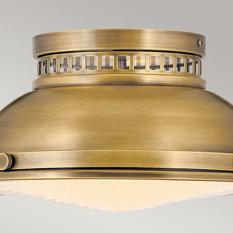 Close-up view of the Amelia 2 Light Flush Light - Brass, showcasing its vintage design. This fixture has a cylindrical shape with decorative grid-like openings near the top, and its smooth, brushed finish in brass appears mounted on a light grey ceiling.