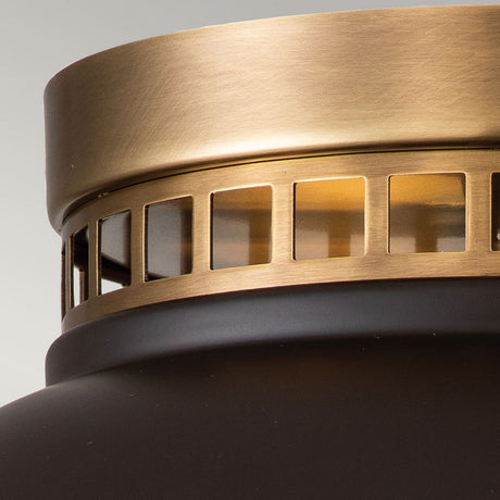 Detailed view of the Amelia 2 Light Flush Light - Bronze, highlighting its bronze and black metallic design. The bronze area features square cutouts that let light filter through, enhancing the soft glow created by the cast glass diffuser. The matte-finished black section stands out against a gently blurred background.