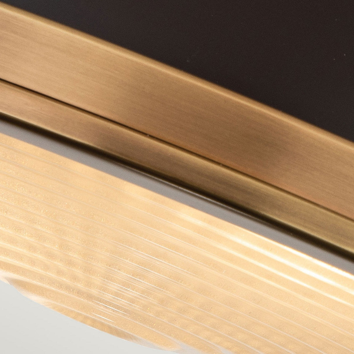 The Amelia 2 Light Flush Light - Bronze showcases an elegant combination of brushed gold and dark metal with gracefully curved lines and grooves, accentuated by a sophisticated bronze finish. The design emphasizes the contrasting textures of the materials, further enriched by the stylish inclusion of a cast glass diffuser.