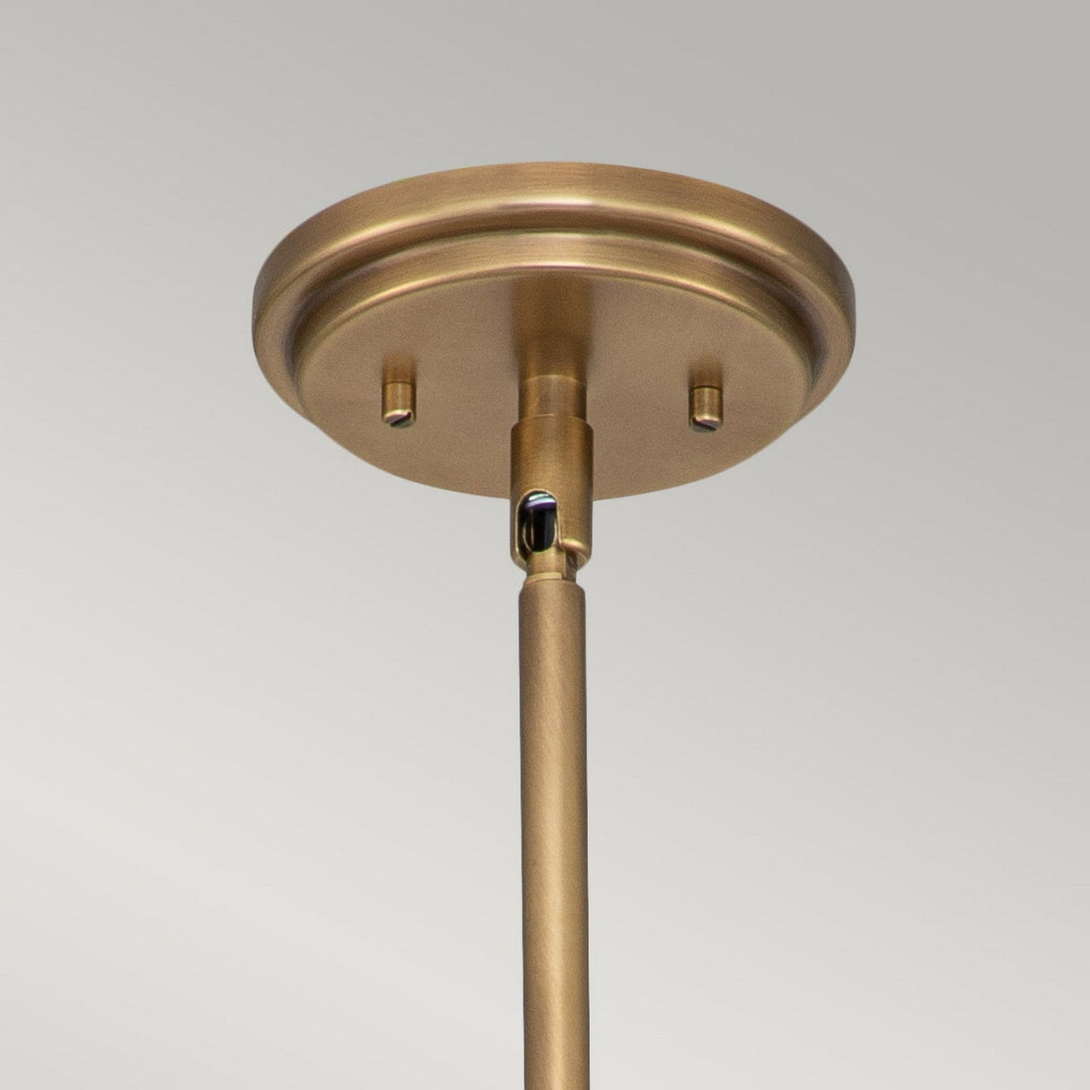 Close-up of the "Amelia 1 Light Medium Pendant - Brass" showcasing a brushed brass finish with vintage charm, featuring a cylindrical rod extending downwards. The pendant includes a round base that enhances its modern farmhouse appeal, set against a light gray background.