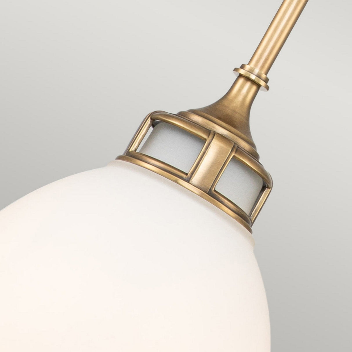 A close-up of the Amelia 1 Light Medium Pendant in Brass, showcasing its frosted glass shade that exudes vintage charm. The pendant features decorative cutouts near the top, blending modern farmhouse elegance against a plain background to accentuate its sophisticated yet timeless appeal.