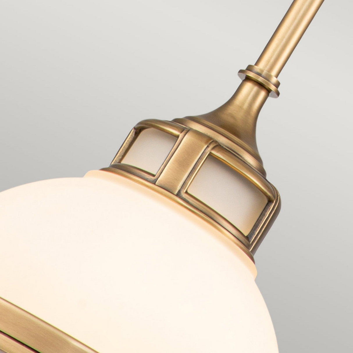 A close-up of the Amelia 1 Light Mini Pendant - Brass highlights its vintage style with an intricate cast glass fitter. The opal glass dome emits a soft, elegant glow, beautifully contrasted against a gray background.