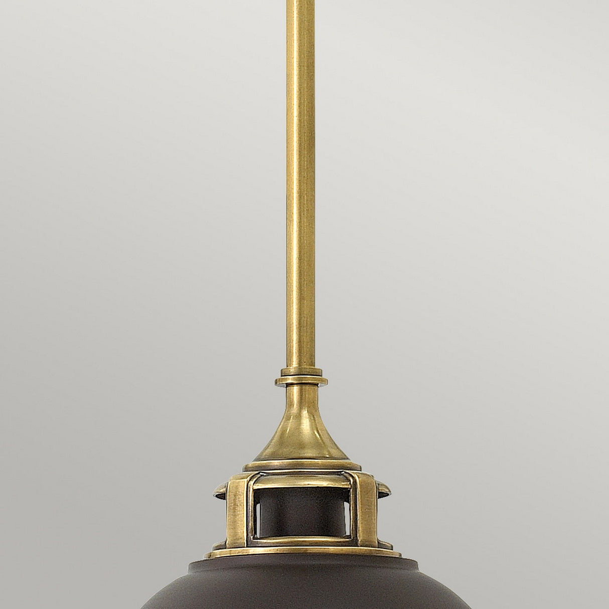 A close-up of the Amelia 1 Light Mini Pendant - Bronze showcases an elegant light fixture with a brass rod and dark metallic shade. Enhanced by its opal glass dome, this bronze lighting piece stands out beautifully against a light gray background.