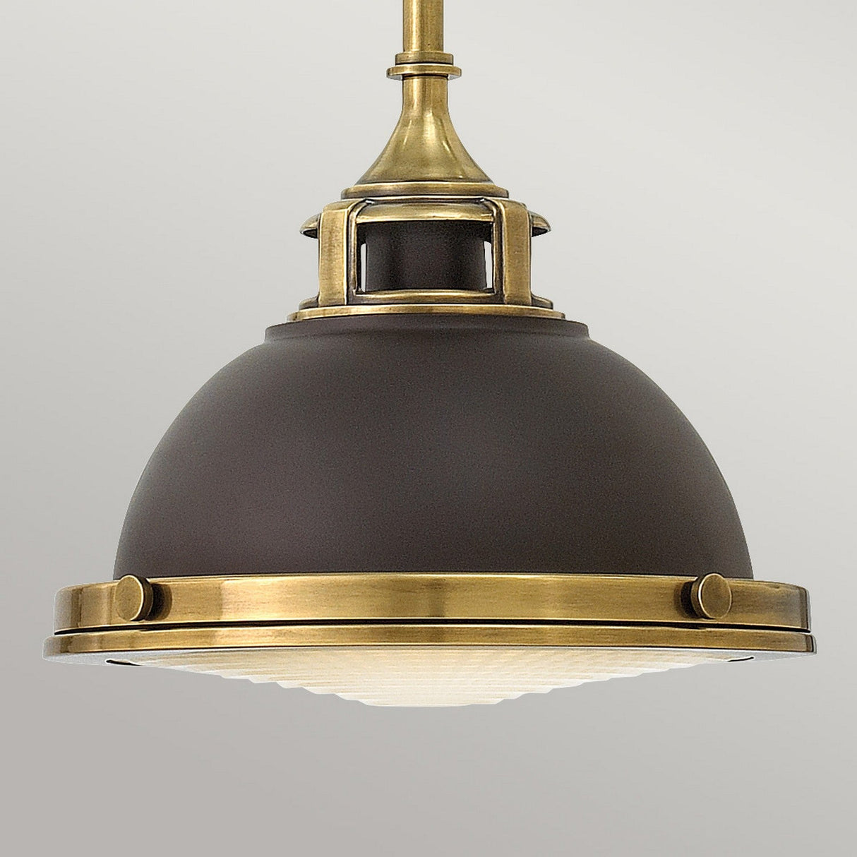 The Amelia 1 Light Mini Pendant - Bronze combines style and functionality with a vintage flair. It showcases a matte black dome paired with brass accents, an intricate brass holder at the top, and a ribbed glass diffuser at the bottom, resulting in a stunning lighting piece for any space.