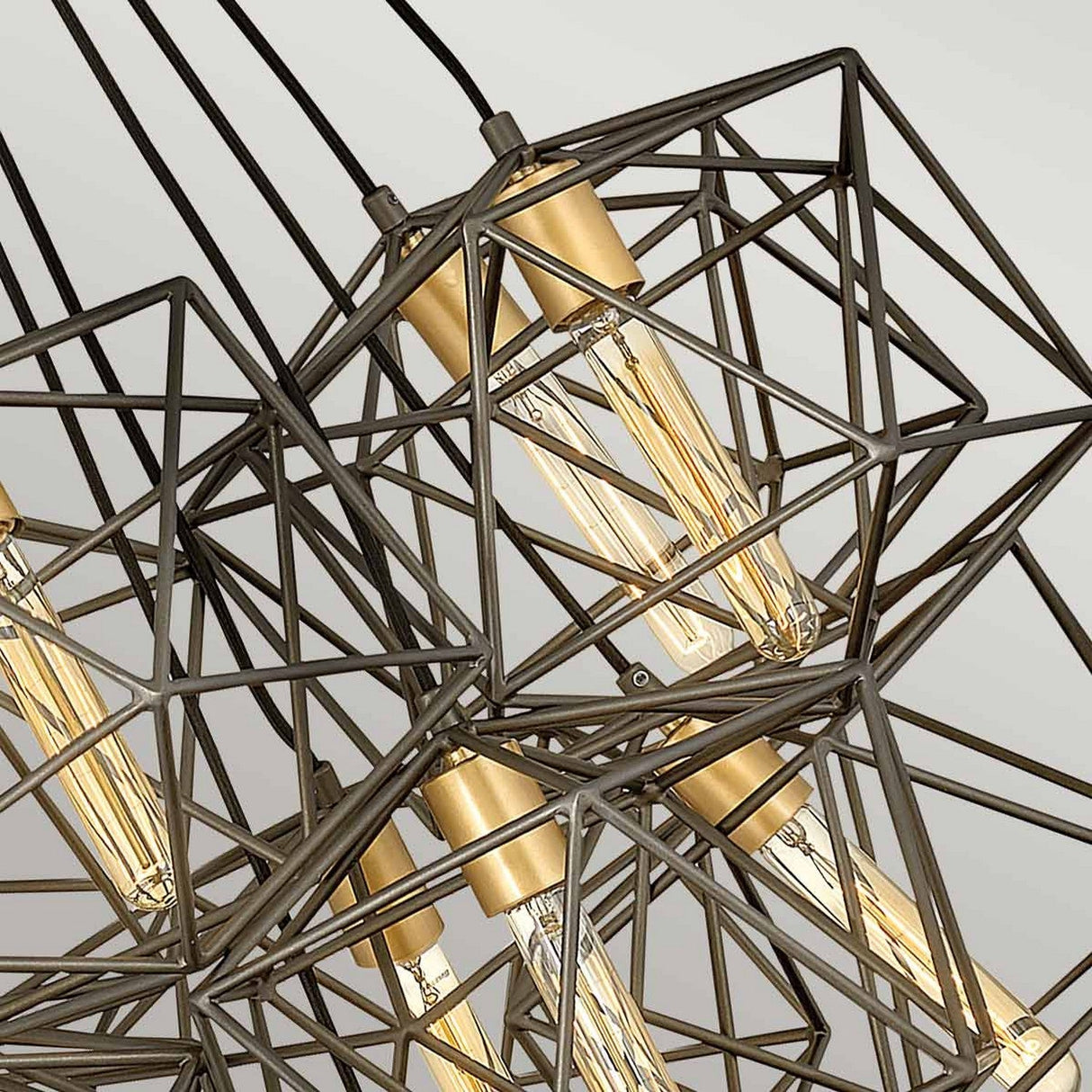 Close-up of the Astrid 11 Light Cluster Pendant, a modern geometric light fixture with several Edison bulbs encased in angular metal wireframes. Its matte bronze and gold finish beautifully highlights the intricate, industrial design against a neutral background.