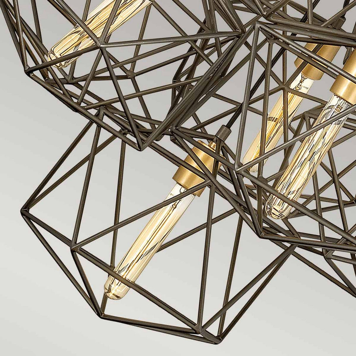 Close-up of the Astrid 11 Light Cluster Pendant in matte bronze and gold, showcasing multiple exposed LED filament bulbs. The geometric chandelier's intricate metal rods form diamond-shaped frames around each bulb, offering a modern and industrial aesthetic against a light gray background.