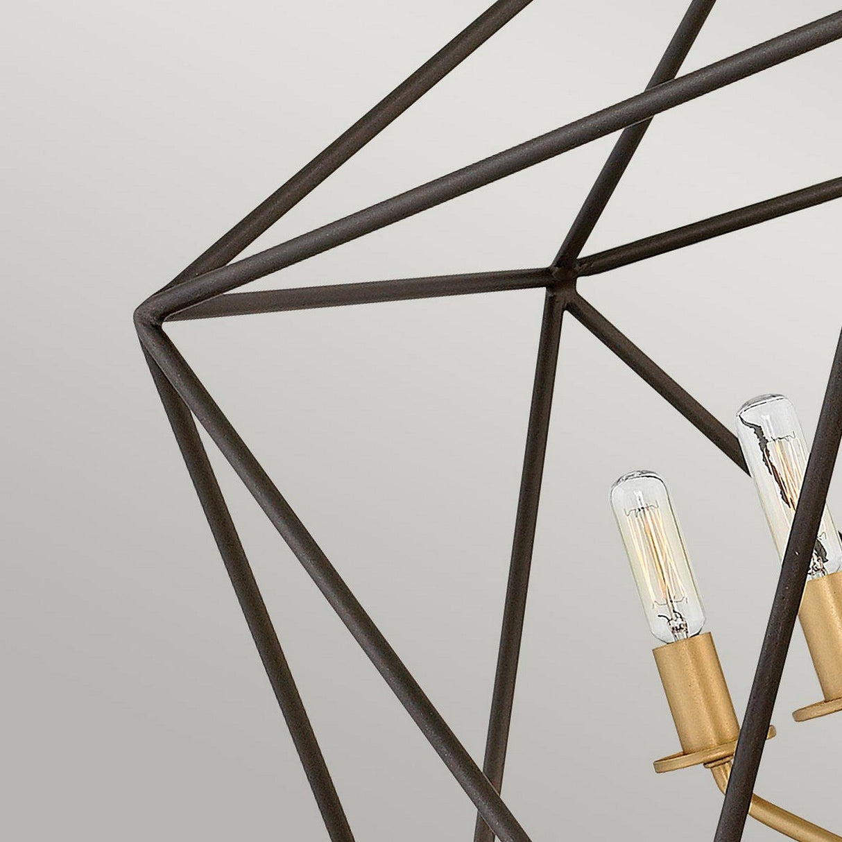 Close-up of a geometric outer cage chandelier enclosing two exposed filament light bulbs with a brushed gold finish against a light grey background, capturing the elegance of an Astrid 5 Light Chandelier in Matte Bronze & Gold.